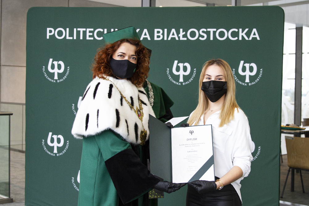 W centrum JM Rektor Marta Kosior Kazberuk i laureatka Gabriela Druć trzymają wspólnie dyplom najlepszego studenta WE. W tle zielony baner Politechniki Białostockiej.