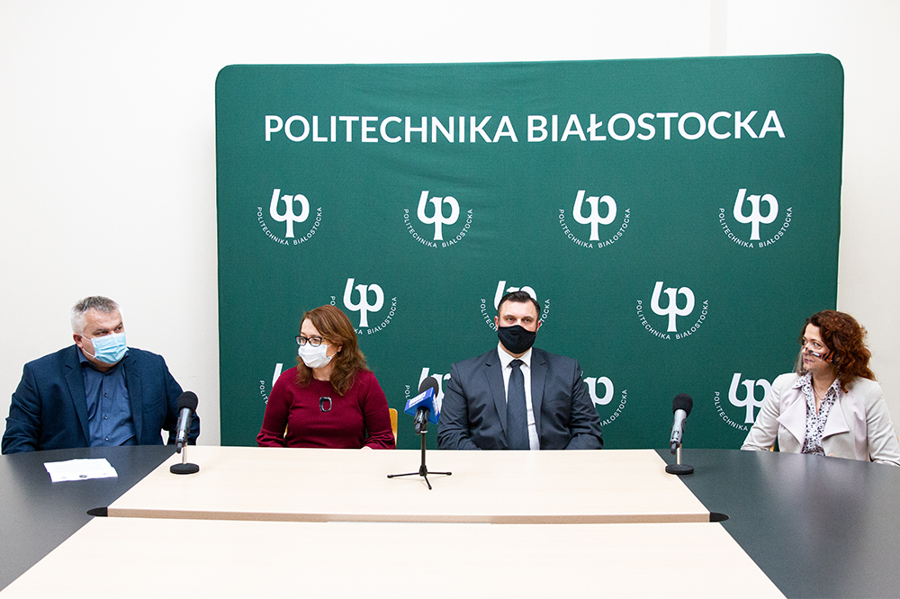 Uczestnicy konferencji siedzą za stołem z ustawionymi mikrofonami.